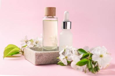 Photo of Stylish presentation of bottles with cosmetic products and beautiful flowers on pink background, closeup