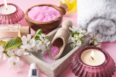 Photo of Spa composition with cosmetic products, burning candles and beautiful flowers on pink background, closeup