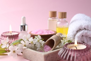 Photo of Spa composition with cosmetic products, burning candles and beautiful flowers on pink background, closeup