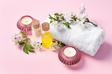 Photo of Spa composition with cosmetic products, burning candles and twigs with beautiful flowers on pink background