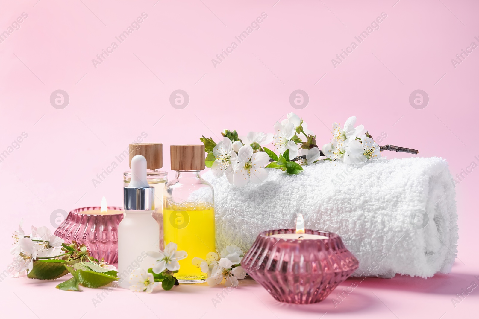 Spa composition with cosmetic products, burning candles and twigs with beautiful flowers on pink background, closeup Photo of Spa composition with cosmetic products, burning candles and twigs with beautiful flowers on pink background, closeup