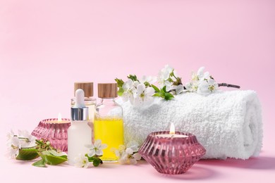 Photo of Spa composition with cosmetic products, burning candles and twigs with beautiful flowers on pink background, closeup