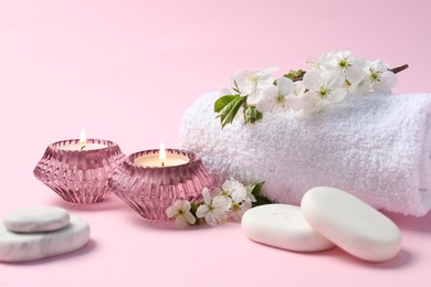 Photo of Spa composition with burning candles, pebble stones and twigs with beautiful flowers on pink background, closeup