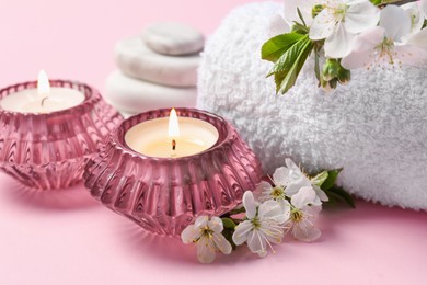 Photo of Spa composition with burning candles, pebble stones and twigs with beautiful flowers on pink background, closeup