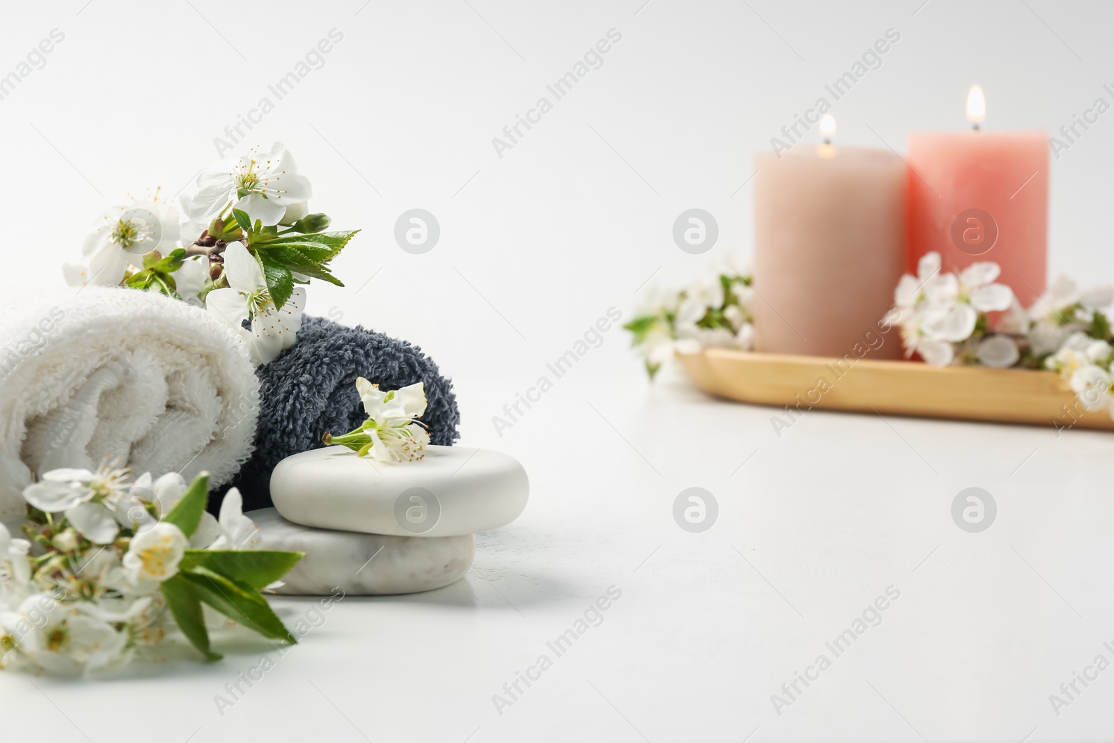 Spa composition with pebble stones, beautiful flowers and burning candles on white background, selective focus Photo of Spa composition with pebble stones, beautiful flowers and burning candles on white background, selective focus