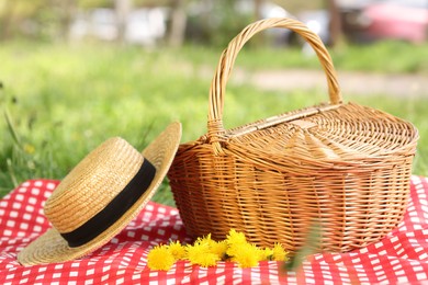 Photo of Wicker basket, dandelion flowers, straw hat and blanket on green grass outdoors