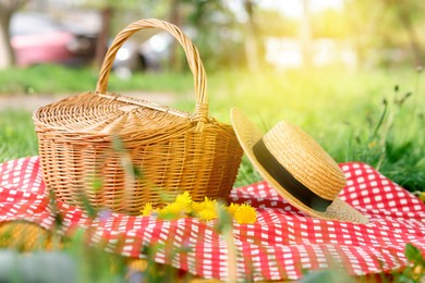 Photo of Wicker basket, dandelion flowers, straw hat and blanket on green grass outdoors