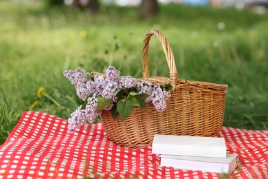 Photo of Books, blanket and wicker basket with lilac flowers on green grass outdoors