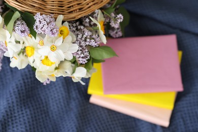 Photo of Stacked books and wicker basket with flowers on blanket, flat lay