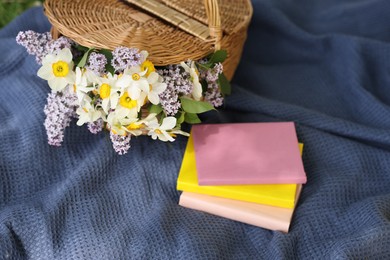 Photo of Stacked books and wicker basket with flowers on blanket outdoors