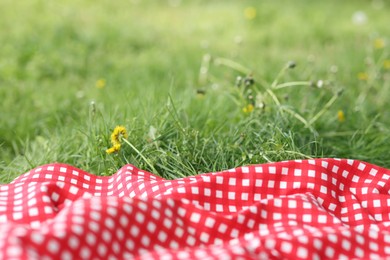 Photo of Red checkered blanket for picnic on green grass outdoors, closeup