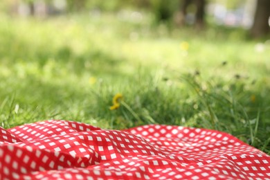 Photo of Red checkered blanket for picnic on green grass outdoors, closeup