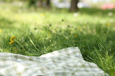 Photo of Checkered blanket for picnic on green grass outdoors, closeup
