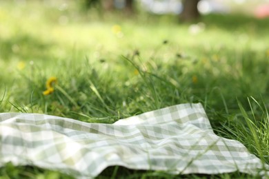 Photo of Checkered blanket for picnic on green grass outdoors, closeup