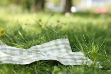 Photo of Checkered blanket for picnic on green grass outdoors, closeup