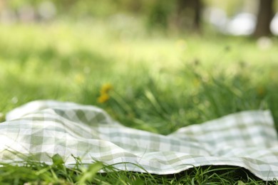 Photo of Checkered blanket for picnic on green grass outdoors, closeup