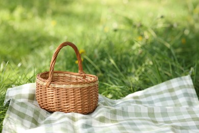 Photo of Wicker basket and blanket on green grass outdoors. Space for text