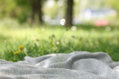 Photo of Light grey blanket for picnic on green grass outdoors, closeup