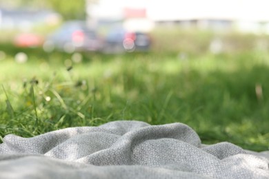 Photo of Light grey blanket for picnic on green grass outdoors, closeup
