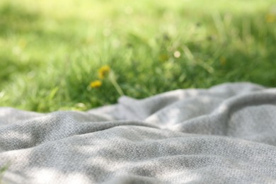 Photo of Light grey blanket for picnic on green grass outdoors, closeup