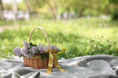 Photo of Wicker basket with lilac flowers on blanket outdoors. Space for text