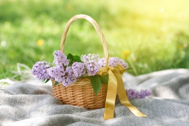Photo of Wicker basket with lilac flowers on blanket outdoors, closeup