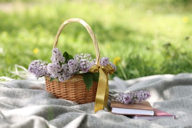 Photo of Stacked books and wicker basket with lilac flowers on green grass outdoors