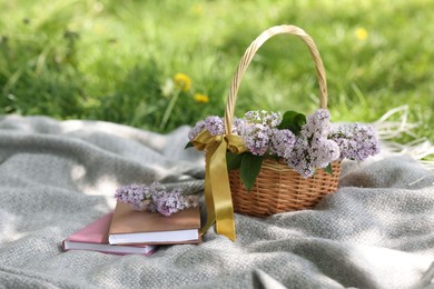 Photo of Stacked books and wicker basket with lilac flowers on green grass outdoors