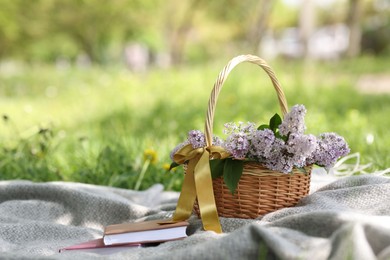 Photo of Stacked books and wicker basket with lilac flowers on green grass outdoors