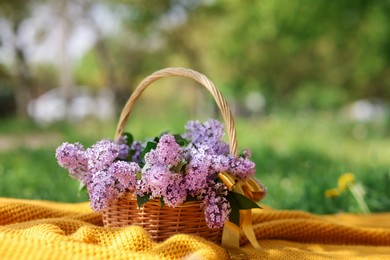 Photo of Wicker basket with lilac flowers on blanket outdoors, closeup