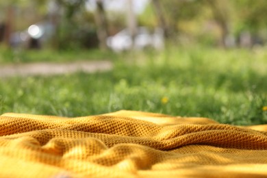 Photo of Orange blanket for picnic on green grass outdoors, closeup