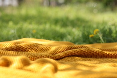 Photo of Orange blanket for picnic on green grass outdoors, closeup