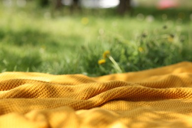 Photo of Orange blanket for picnic on green grass outdoors, closeup