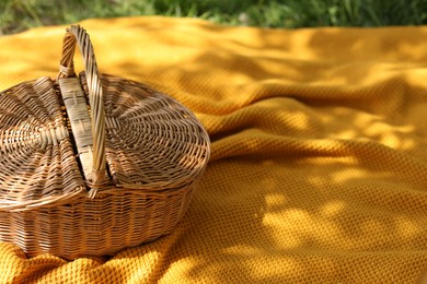 Photo of Wicker basket and blanket on green grass outdoors, closeup