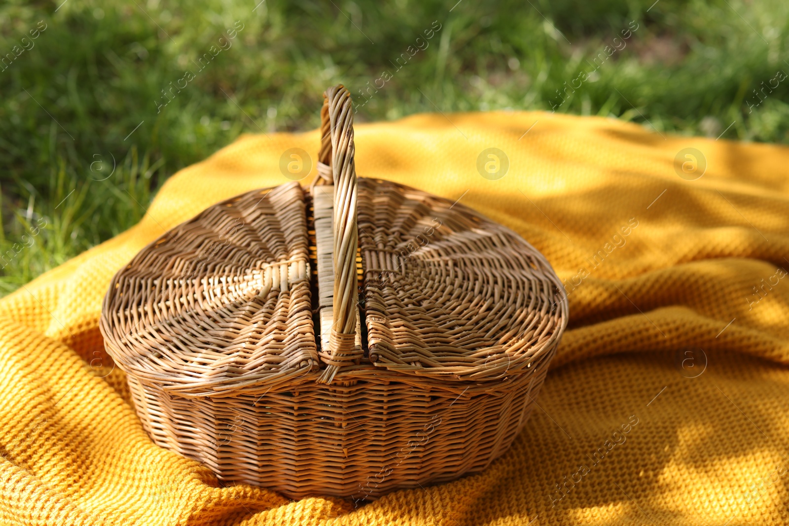 Wicker basket and blanket on green grass outdoors, closeup Photo of Wicker basket and blanket on green grass outdoors, closeup