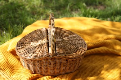 Photo of Wicker basket and blanket on green grass outdoors, closeup