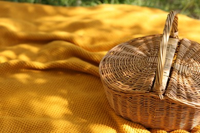 Photo of Wicker basket and blanket on green grass outdoors, closeup