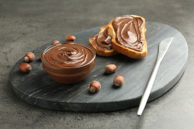 Photo of Toasts with tasty chocolate spread and hazelnuts on gray textured table, closeup