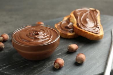 Photo of Tasty chocolate spread, toasts and hazelnuts on gray table, closeup