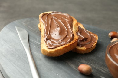 Photo of Toasts with tasty chocolate spread and hazelnuts on gray table, closeup