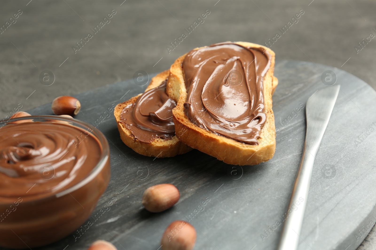 Photo of Toasts with tasty chocolate spread and hazelnuts on gray table, closeup