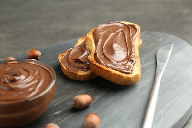 Photo of Toasts with tasty chocolate spread and hazelnuts on gray table, closeup