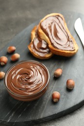 Photo of Tasty chocolate spread, toasts and hazelnuts on gray table, closeup
