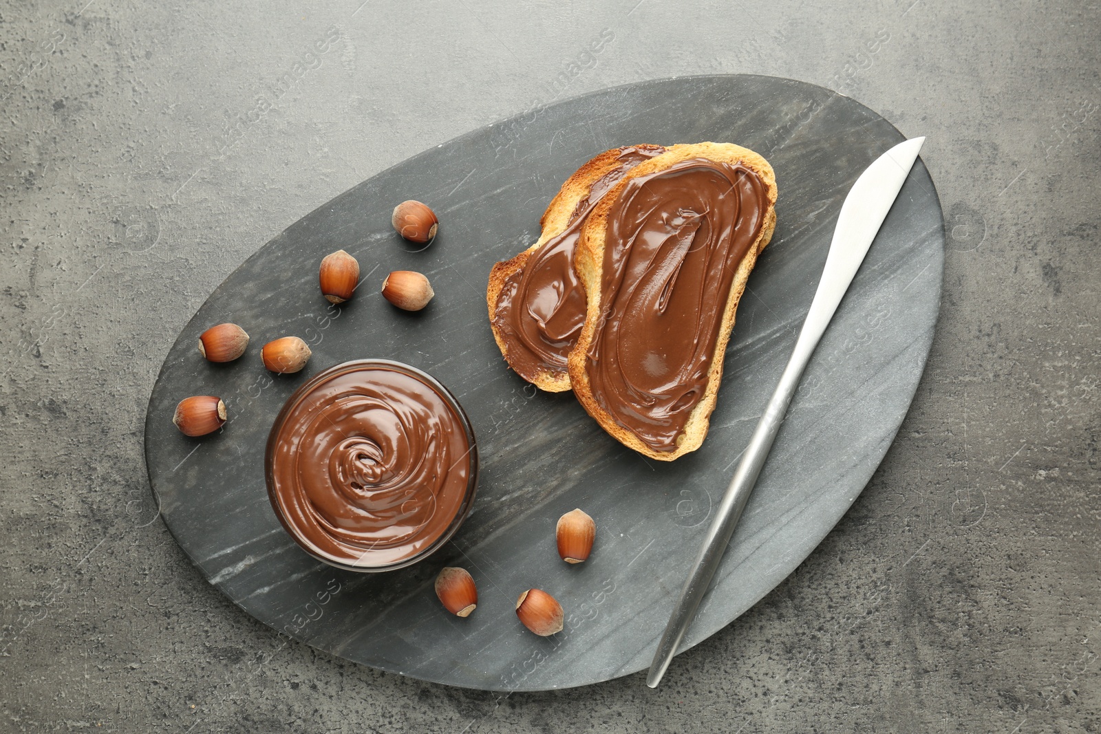 Toasts with tasty chocolate spread and hazelnuts on gray textured table, top view Photo of Toasts with tasty chocolate spread and hazelnuts on gray textured table, top view