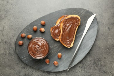Photo of Toasts with tasty chocolate spread and hazelnuts on gray textured table, top view