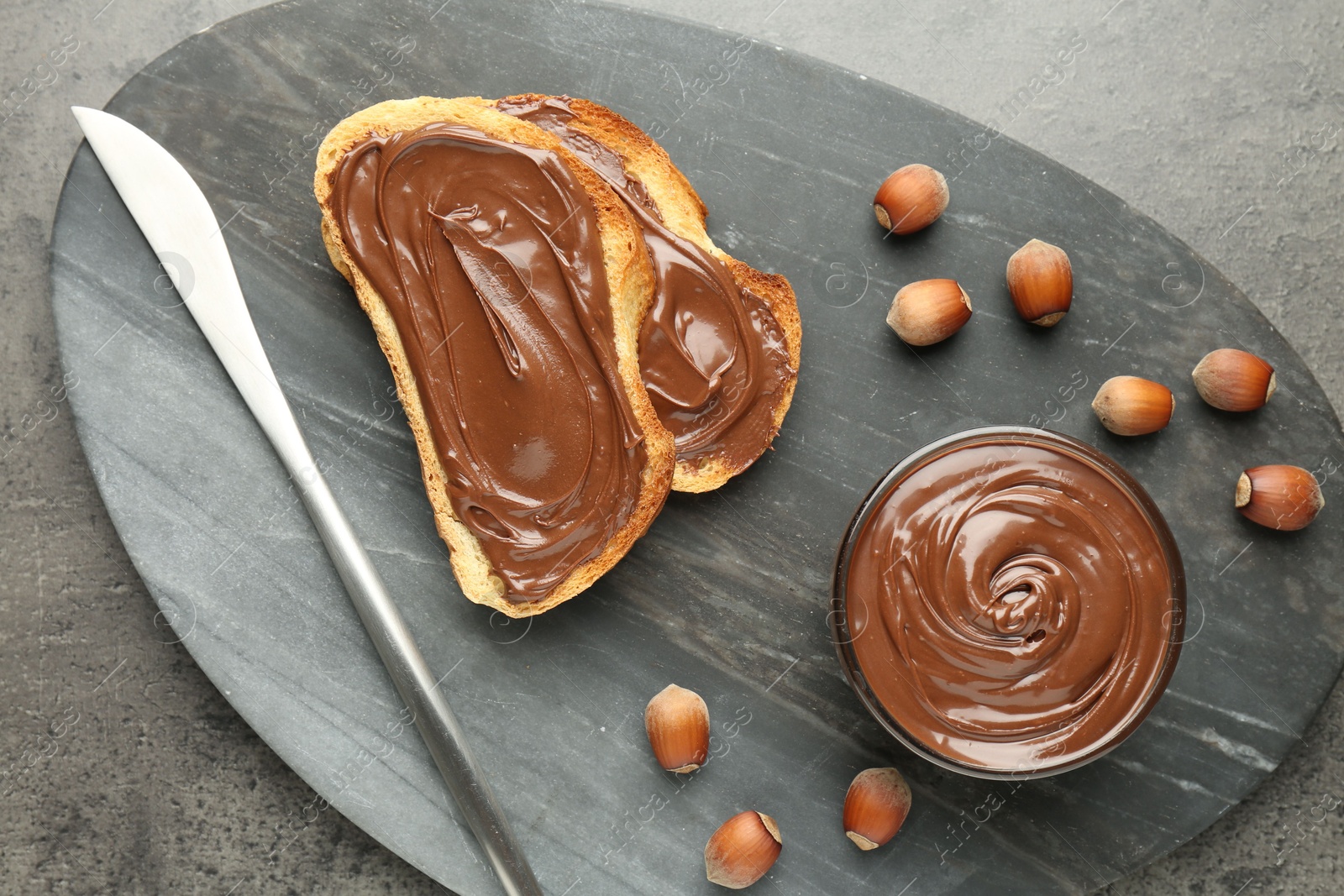 Toasts with tasty chocolate spread and hazelnuts on gray textured table, top view Photo of Toasts with tasty chocolate spread and hazelnuts on gray textured table, top view