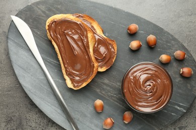 Photo of Toasts with tasty chocolate spread and hazelnuts on gray textured table, top view