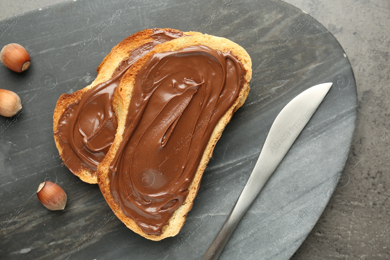 Toasts with tasty chocolate spread and hazelnuts on gray textured table, top view Photo of Toasts with tasty chocolate spread and hazelnuts on gray textured table, top view