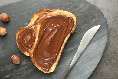 Photo of Toasts with tasty chocolate spread and hazelnuts on gray textured table, top view