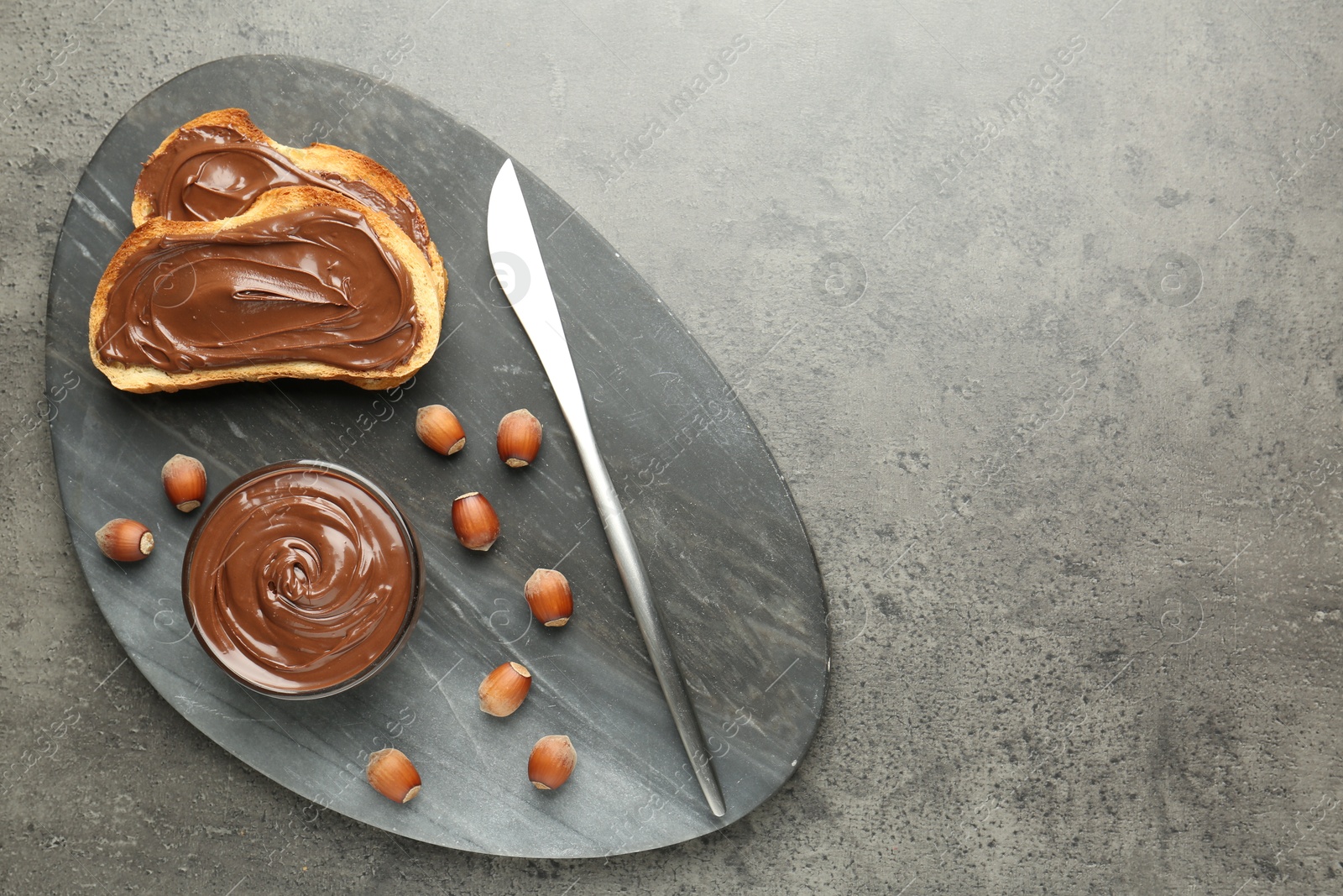 Photo of Toasts with tasty chocolate spread and hazelnuts on gray textured table, top view. Space for text